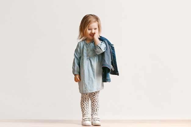 Portrait de toute la longueur de la petite fille mignonne enfant dans des vêtements de jeans élégants et souriant, debout sur blanc. Concept de mode pour enfants