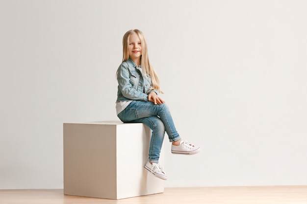 Portrait de toute la longueur de la petite fille mignonne enfant dans des vêtements de jeans élégants et souriant, debout sur blanc. Concept de mode pour enfants