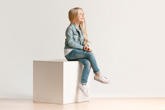 Portrait de toute la longueur de la petite fille mignonne enfant dans des vêtements de jeans élégants et souriant, debout sur blanc. Concept de mode pour enfants