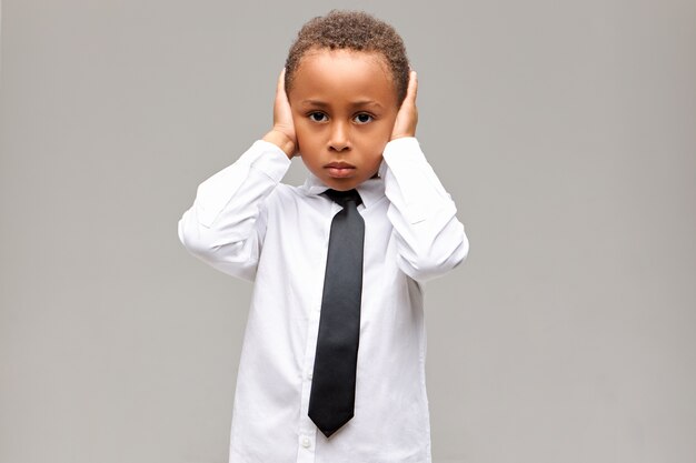 Portrait de triste malheureux garçon afro-américain en uniforme scolaire ayant bouleversé l'expression du visage déprimé, couvrant les oreilles avec les mains, ne supporte pas les parents qui se battent. Langage corporel, réaction et sentiments