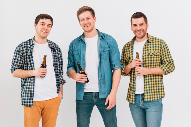 Portrait de trois amis souriants tenant des bouteilles de bière à la main en regardant la caméra