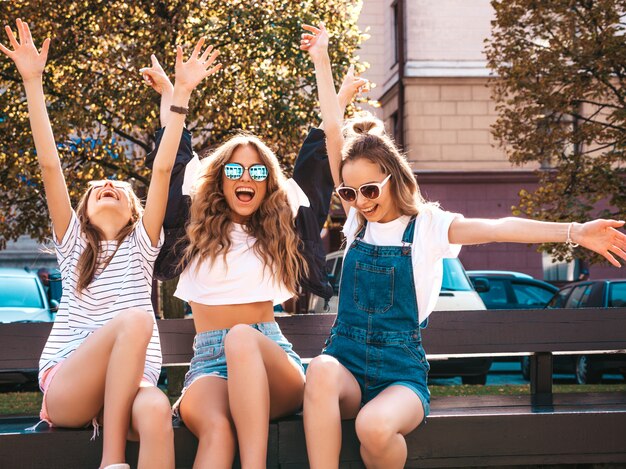 Portrait, de, trois, jeune, beau, sourire, hipster, filles, dans, branché, vêtements été., Sexy, insouciant, femmes, séance banc, dans, les, street., Positif, modèles, amusant, dans, sunglasses., Lever mains