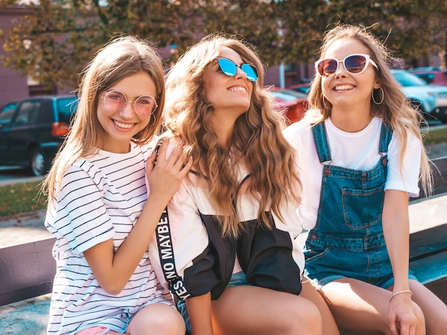 Portrait de trois jeunes belles filles hipster souriantes dans des vêtements d'été à la mode. Sexy, insouciant, femmes, poser, rue, positif, modèles, amusant, lunettes soleil, étreindre