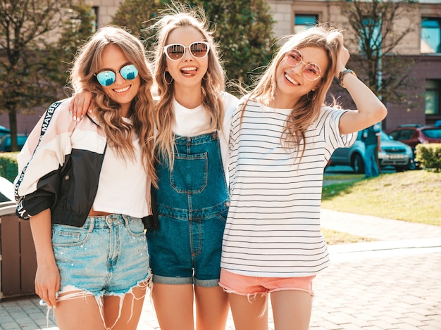 Portrait de trois jeunes belles filles hipster souriantes dans des vêtements d'été à la mode. Sexy, insouciant, femmes, poser, rue, positif, modèles, amusant, lunettes soleil, étreindre