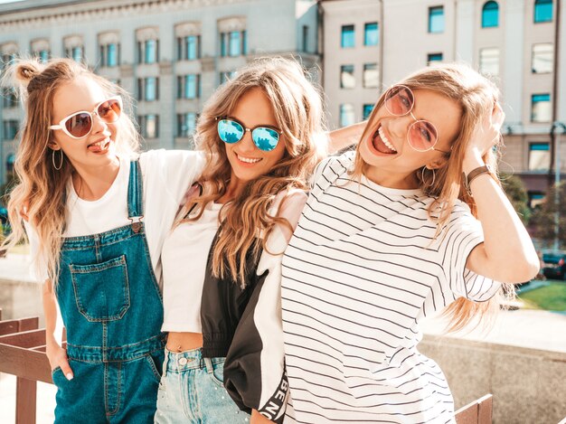 Portrait de trois jeunes belles filles hipster souriantes dans des vêtements d'été à la mode. Sexy, insouciant, femmes, poser, rue, positif, modèles, amusant, lunettes soleil, étreindre