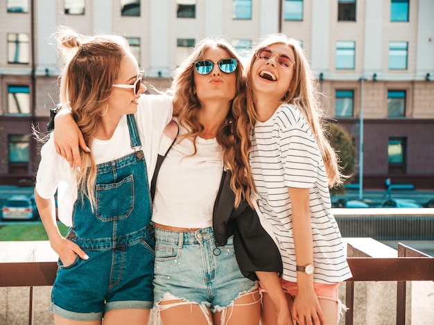 Portrait de trois jeunes belles filles hipster souriantes dans des vêtements d'été à la mode. Sexy, insouciant, femmes, poser, rue, positif, modèles, amusant, lunettes soleil, étreindre