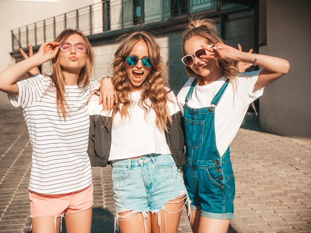 Portrait de trois jeunes belles filles hipster souriantes dans des vêtements d'été à la mode. Sexy, insouciant, femmes, poser, rue, positif, modèles, amusant, lunettes soleil, étreindre
