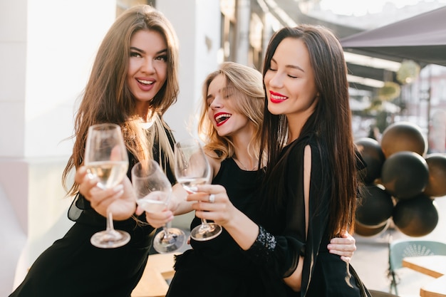 Portrait de trois sœurs en tenue noire célébrant un événement important avec du champagne