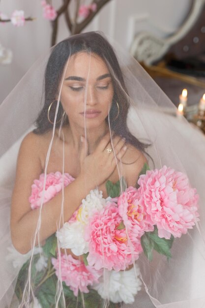 Portrait vertical de jeune femme sous tulle blanc avec bouquet de fleurs Photo de haute qualité