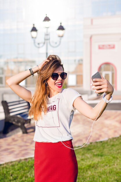 Portrait vertical d'une jeune fille très souriante debout tenant un smartphone et faisant un selfie