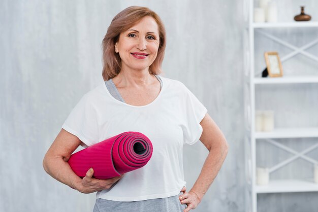 Portrait d&#39;une vieille femme souriante tenant un tapis d&#39;yoga roulé