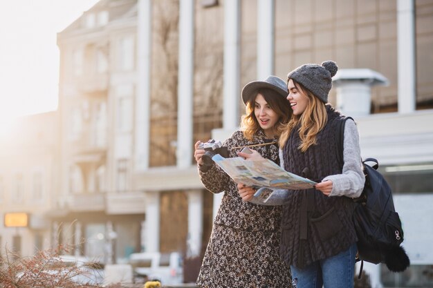 Portrait de ville élégante de deux femmes à la mode marchant dans le centre-ville moderne d'Europe. Amis à la mode voyageant avec sac à dos, carte, appareil photo, prise de photo, touriste, perdez-vous, placez-vous pour le texte.