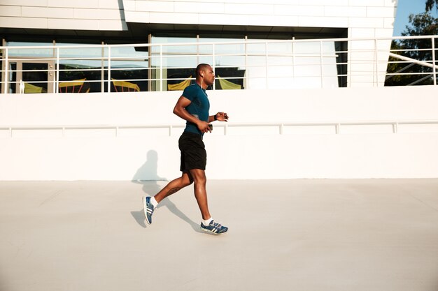 Portrait de vue latérale d'un sportif africain dans les écouteurs en cours d'exécution