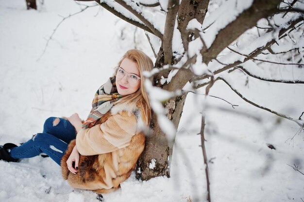 Portraiy de fille blonde à lunettes manteau de fourrure rouge et écharpe au jour d'hiver