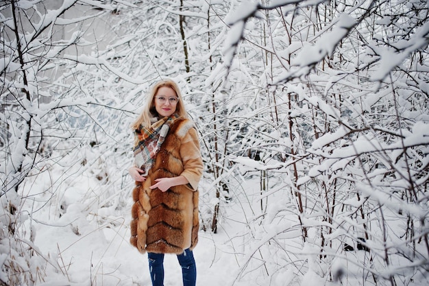 Portraiy de fille blonde à lunettes manteau de fourrure rouge et écharpe au jour d'hiver