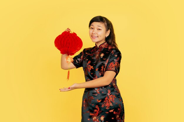 Posant avec lanterne, souriant, invitant. Joyeux Nouvel An chinois. Portrait de jeune fille asiatique sur fond jaune. Copyspace.