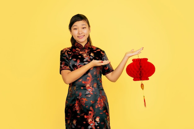 Posant avec lanterne, souriant, invitant. Joyeux Nouvel An chinois. Portrait de jeune fille asiatique sur fond jaune. Copyspace.