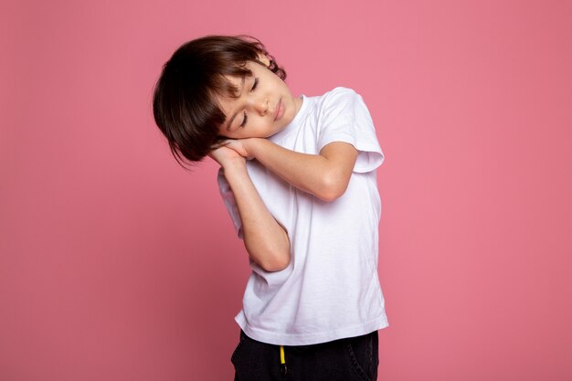Posant petit garçon mignon adorable en t-shirt blanc et pantalon noir sur mur rose