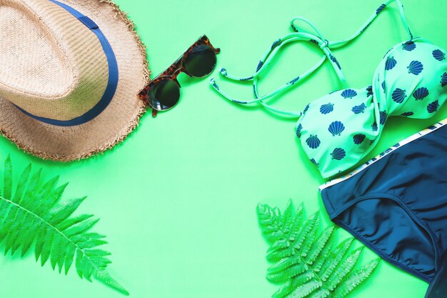 Pose plate de bikini et accessoires avec des feuilles de fougère sur fond vert, concept d&#39;été