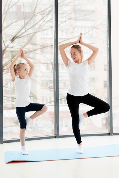 Pose de yoga avec la mère et la fille souriante à la maison