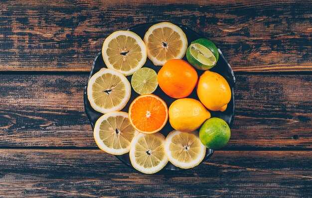 Poser des tranches de citron à plat dans une assiette avec des oranges et du citron vert sur fond de bois foncé. espace horizontal pour le texte