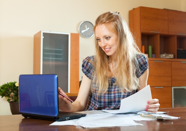 Positive femme aux cheveux longs travaillant avec des documents et un ordinateur portable