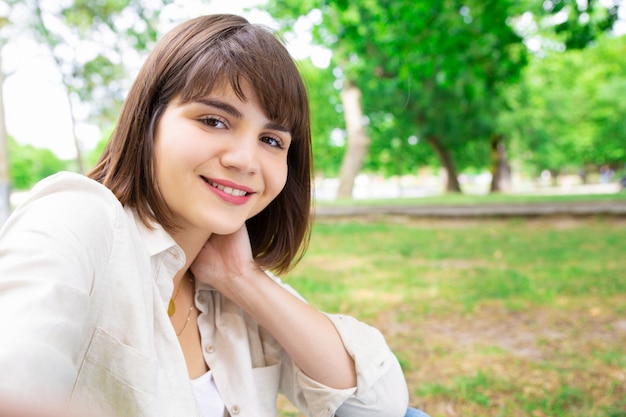 Positive jolie femme prenant selfie photo et assis sur la pelouse