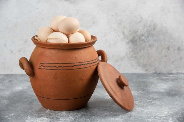 Pot en argile plein d'oeufs de poule crus sur marbre.