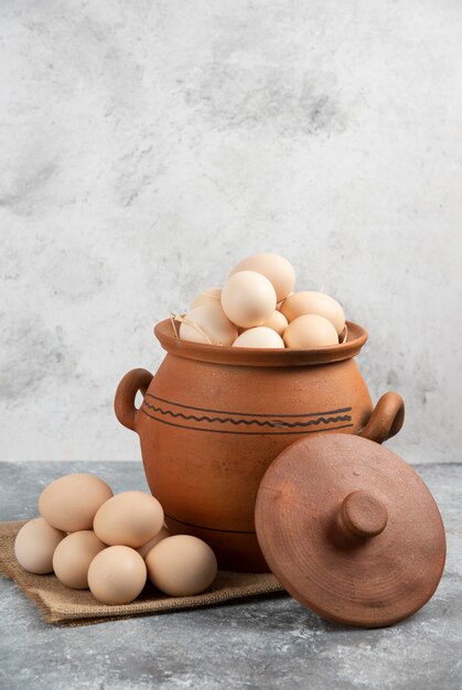 Pot en argile plein d'oeufs de poule crus sur marbre.