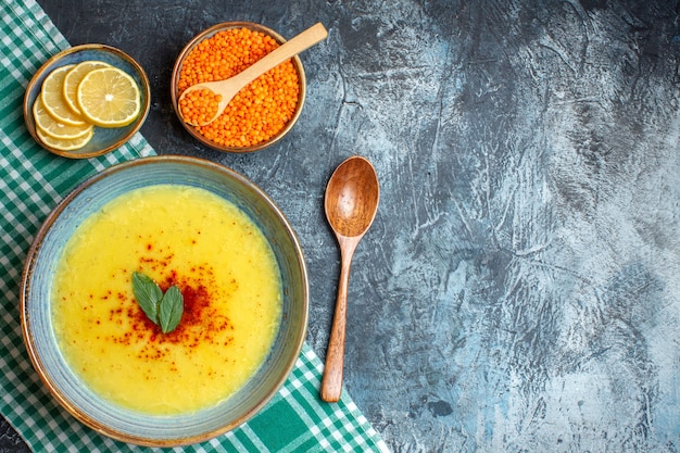 Un pot bleu avec une soupe savoureuse servie avec de la menthe et du poivre à côté d'une cuillère en bois de citron haché et d'un pois jaune sur le côté droit sur fond bleu