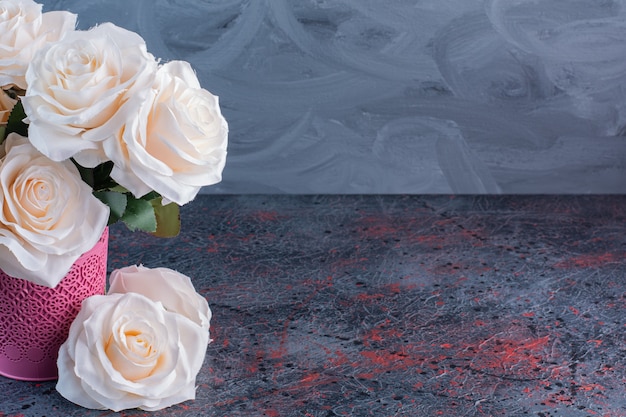 Un pot de fleurs rose avec des fleurs de roses blanches sur fond gris