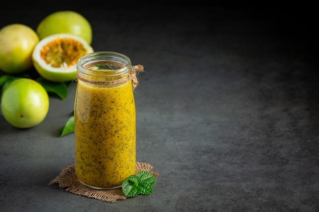 un pot de jus de fruit de la passion et de fruits de la passion frais coupés en deux sur un sol sombre