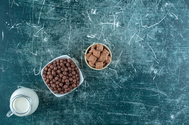 Un pot de lait et de céréales dans des bols , sur la table bleue.