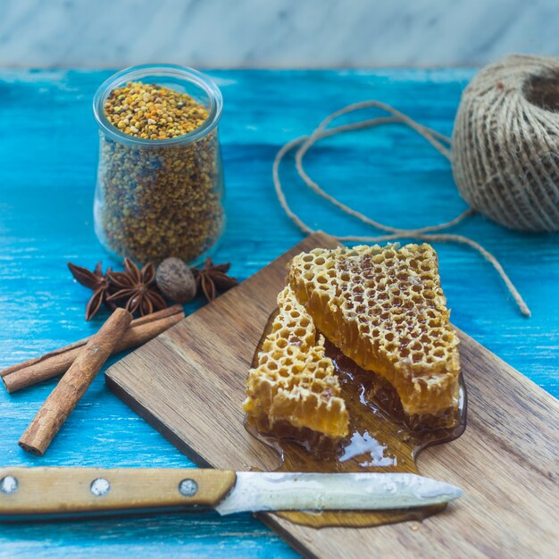 Pot de pollen d&#39;abeille; morceau d&#39;épices et nid d&#39;abeille avec couteau sur planche à découper