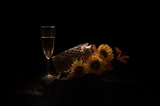 Pot avec des tournesols et un verre de champagne sur la table isolé sur fond noir