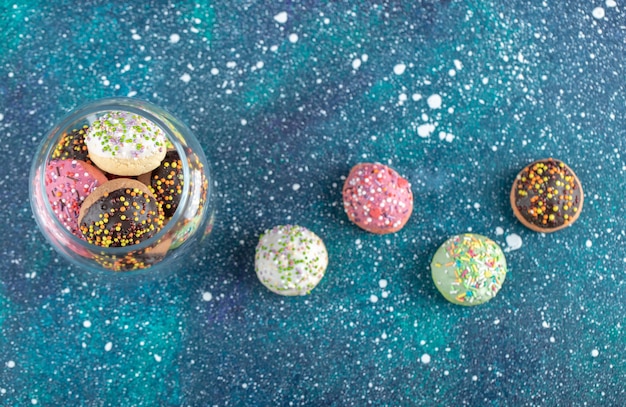 Pot en verre de biscuits saupoudrés colorés sur table bleue.