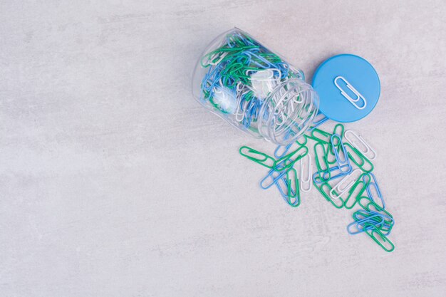 Pot en verre de punaises colorées sur une surface blanche