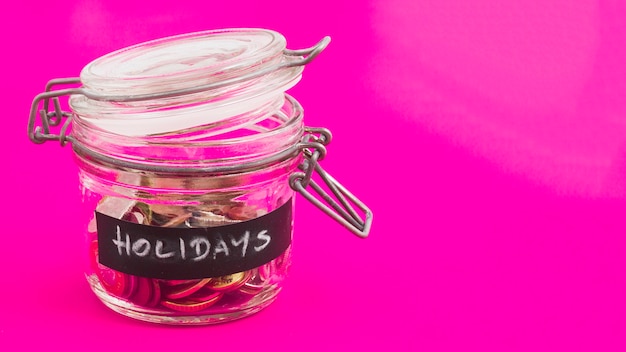 Pot de verre de vacances avec des pièces de monnaie et des billets en euros sur fond rose