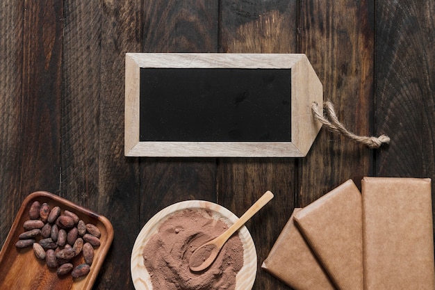 Poudre de cacao, haricots, barre de chocolat enveloppé et petite ardoise en bois sur la table en bois