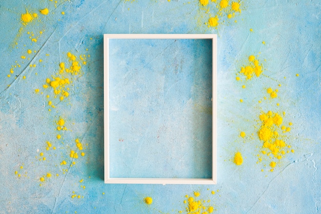 Photo gratuite poudre de couleur jaune autour du cadre de bordure blanche sur un mur peint
