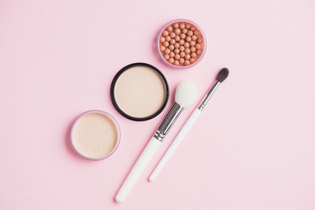 Poudres pour le visage; perles de bronzage et pinceaux de maquillage sur la surface rose