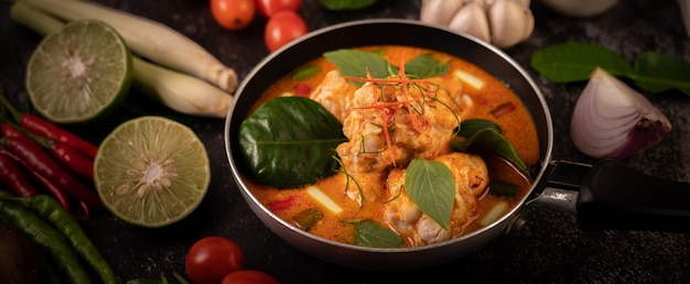 Poulet au curry dans une poêle avec citronnelle, feuilles de lime kaffir, tomates, citron et ail