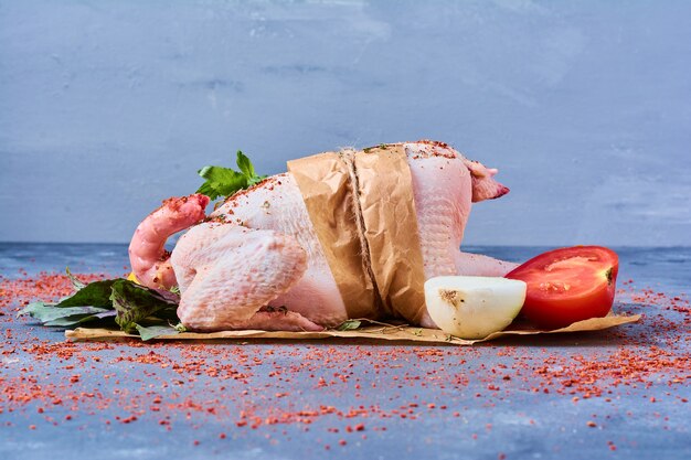 Poulet cru aux herbes sur une planche de bois sur bleu