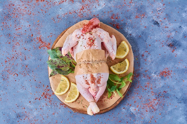 Poulet cru aux herbes sur une planche de bois sur bleu