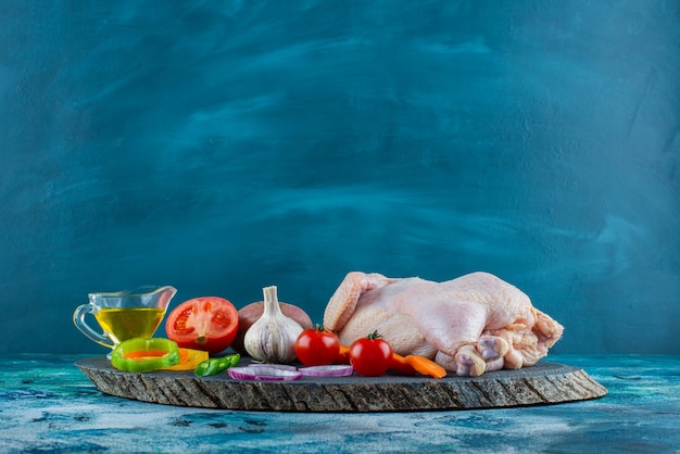 Poulet cru, légumes et huile sur une planche sur la surface bleue