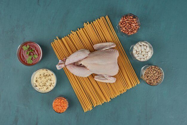 Poulet cru sur une planche de bois avec des haricots et des épices, vue du dessus.