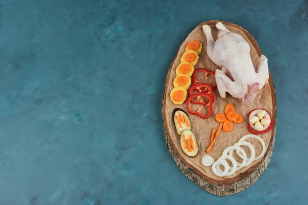 Poulet cru sur une planche de bois avec des légumes.