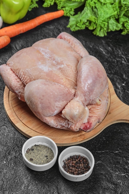 Poulet entier cru sur planche de bois avec des légumes et des épices