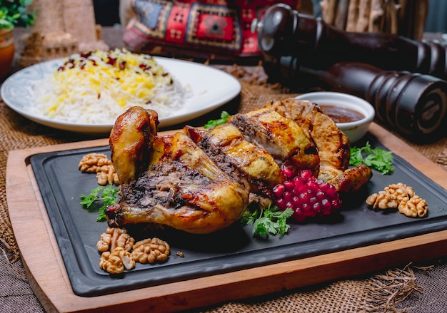 Poulet farci rôti décoré de grenade et de noix sur un tableau noir et de riz dans une assiette blanche sur une table en bois