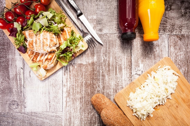 Photo gratuite poulet grillé frais sur planche de bois à côté de pain sain, tomates et salade. mode de vie et alimentation sains